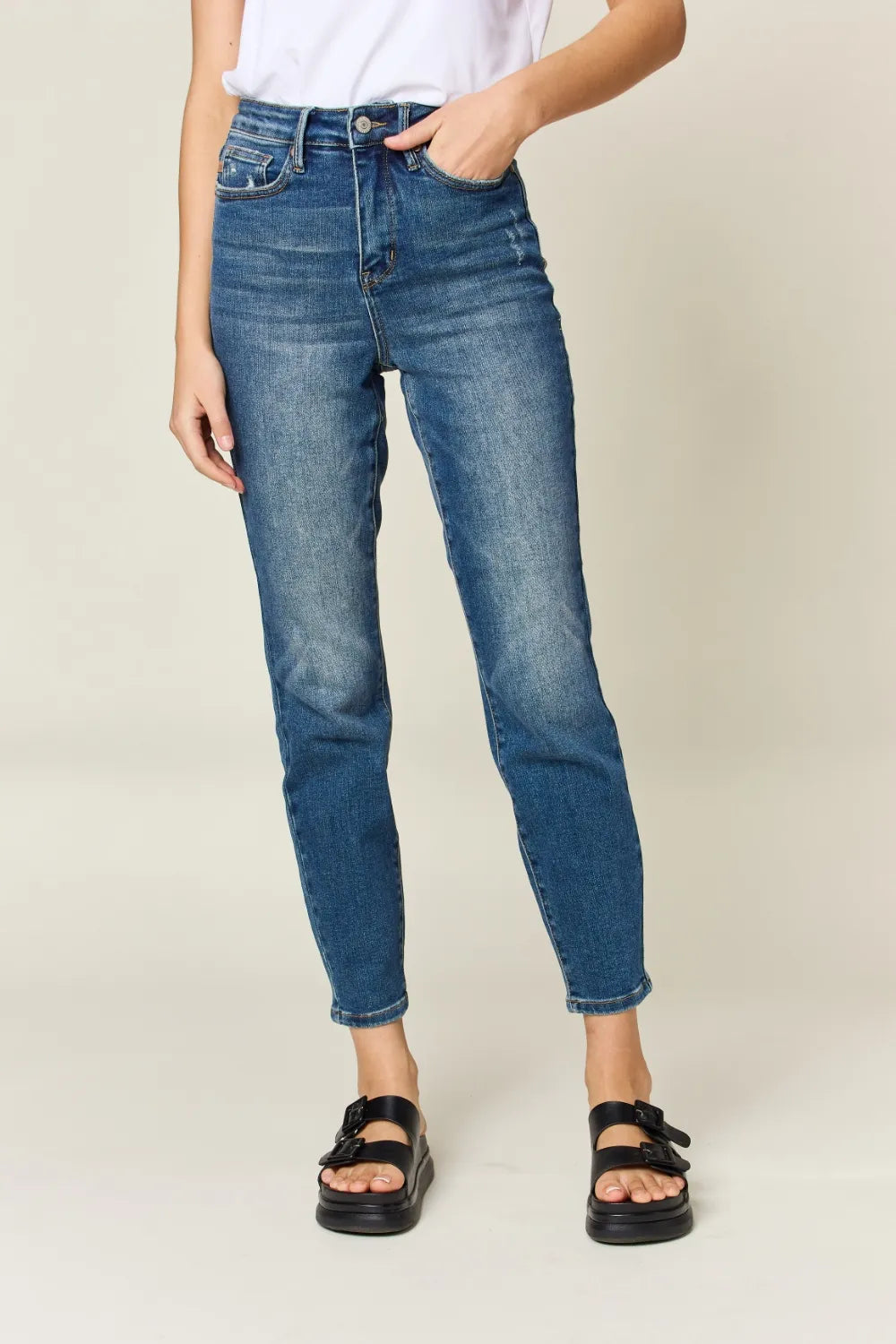 Person wearing blue jeans and black sandals on a plain background
