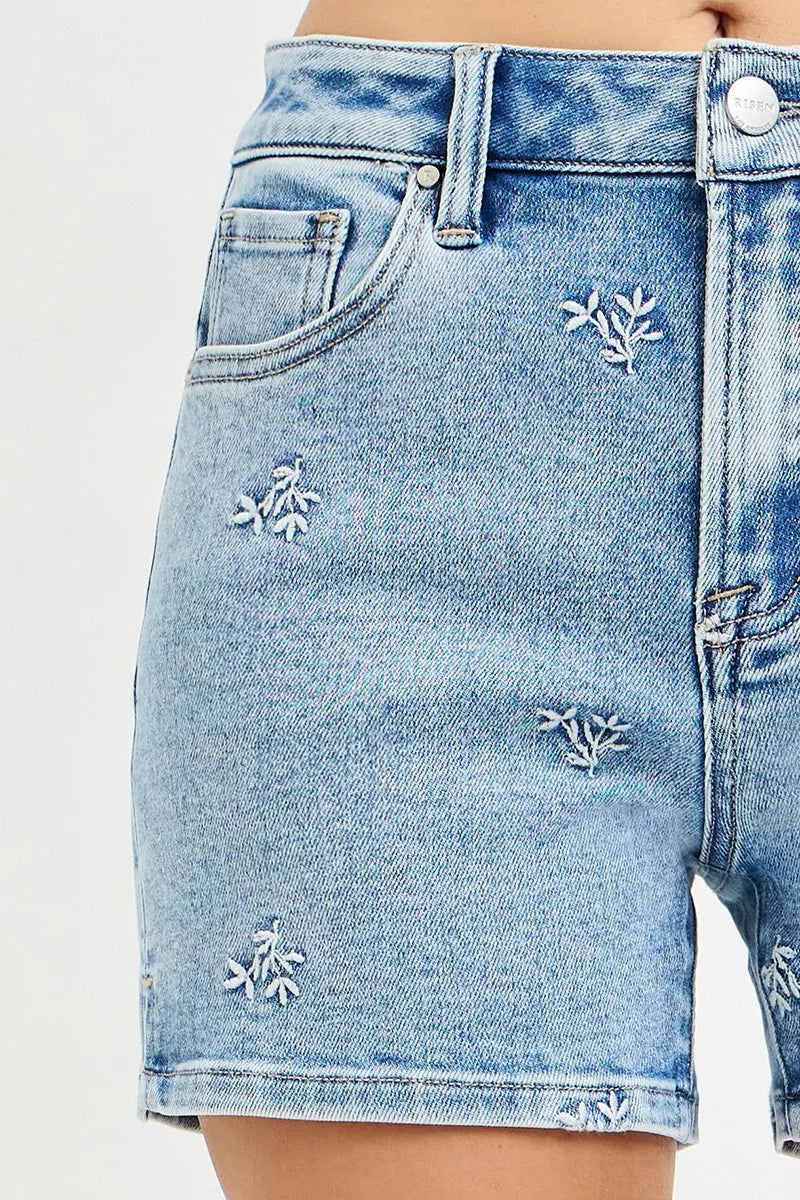 Close-up of light blue denim shorts with floral embroidery on a white background