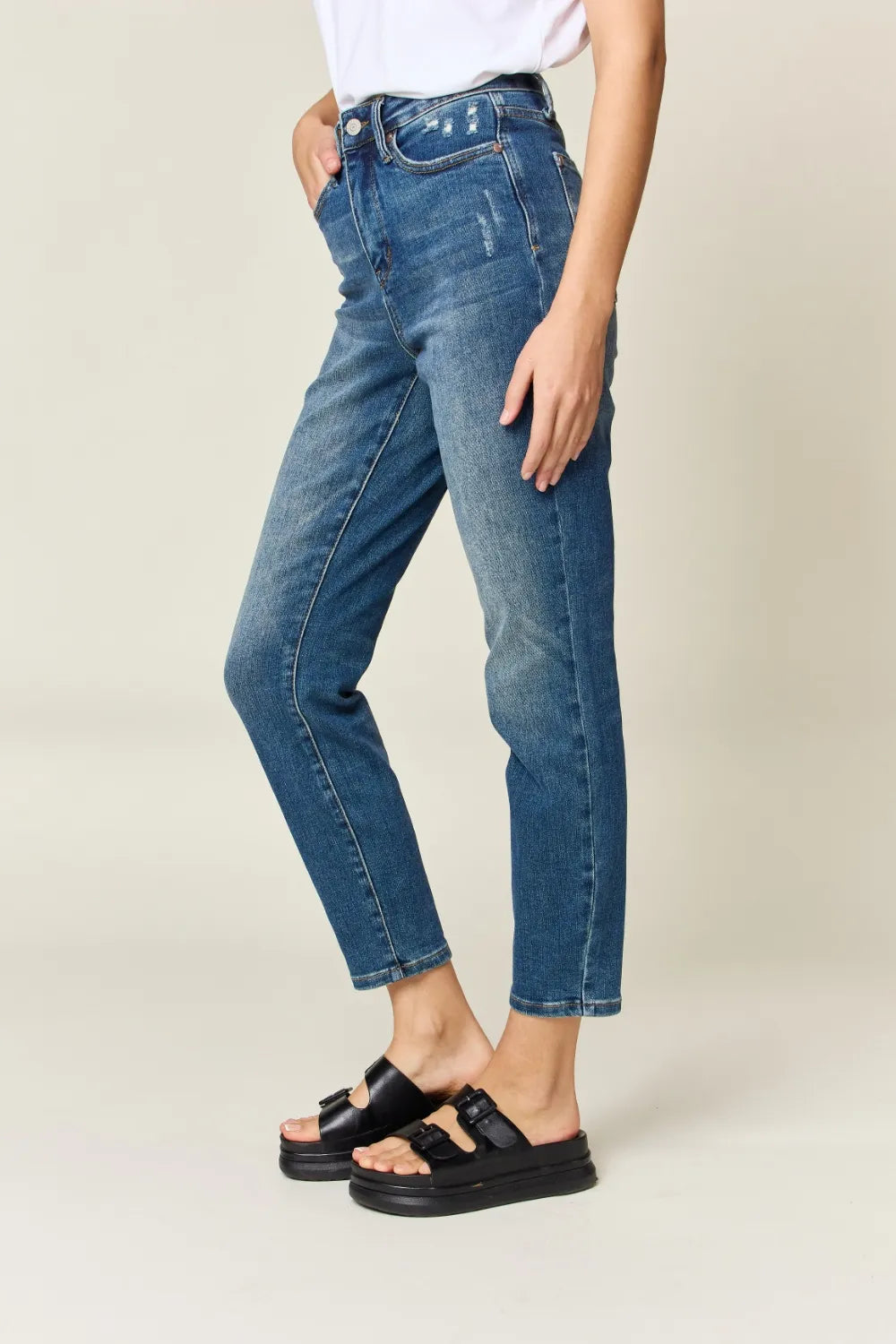 Person wearing blue jeans and black sandals on a plain background