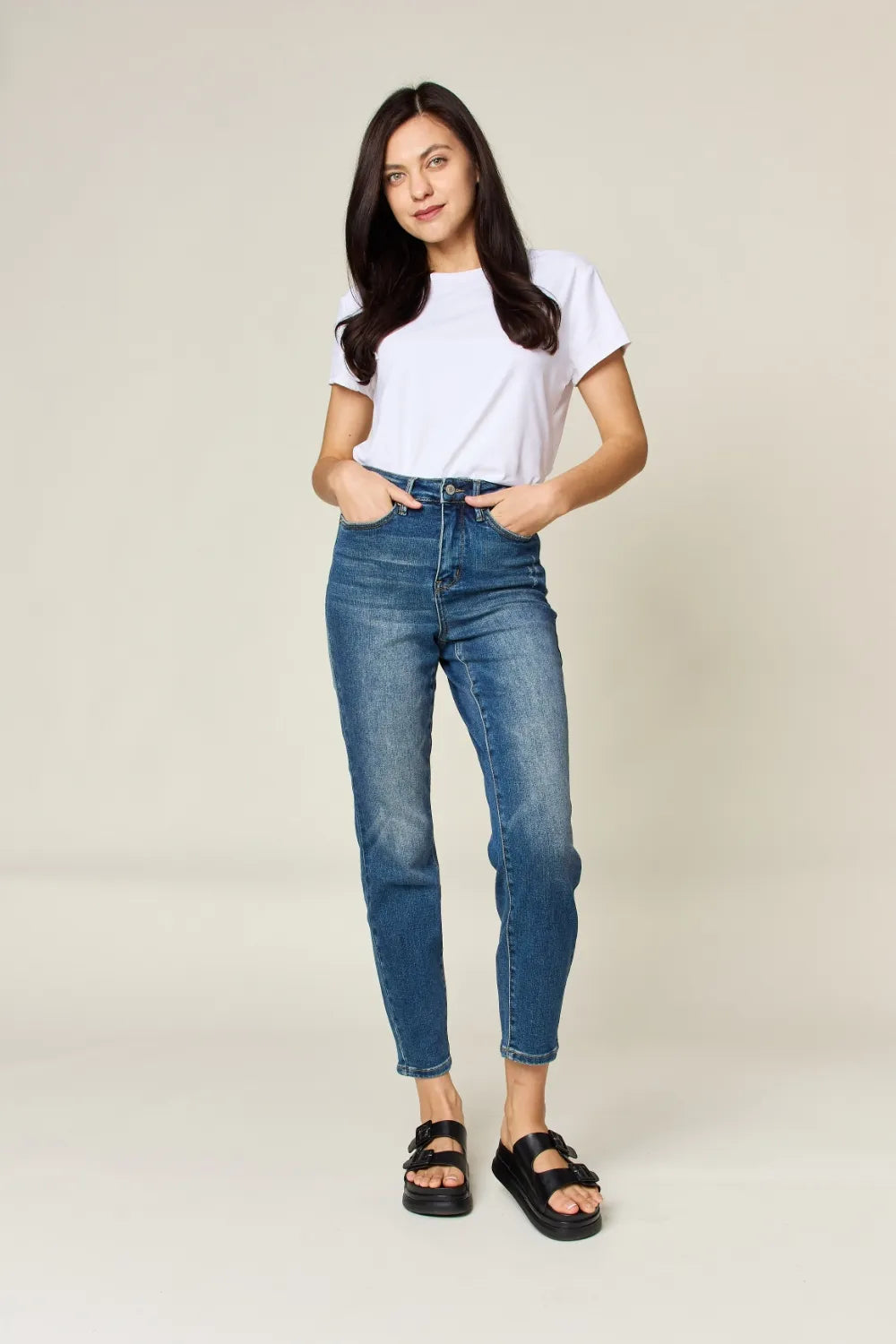 Woman wearing a white t-shirt and blue jeans against a plain background