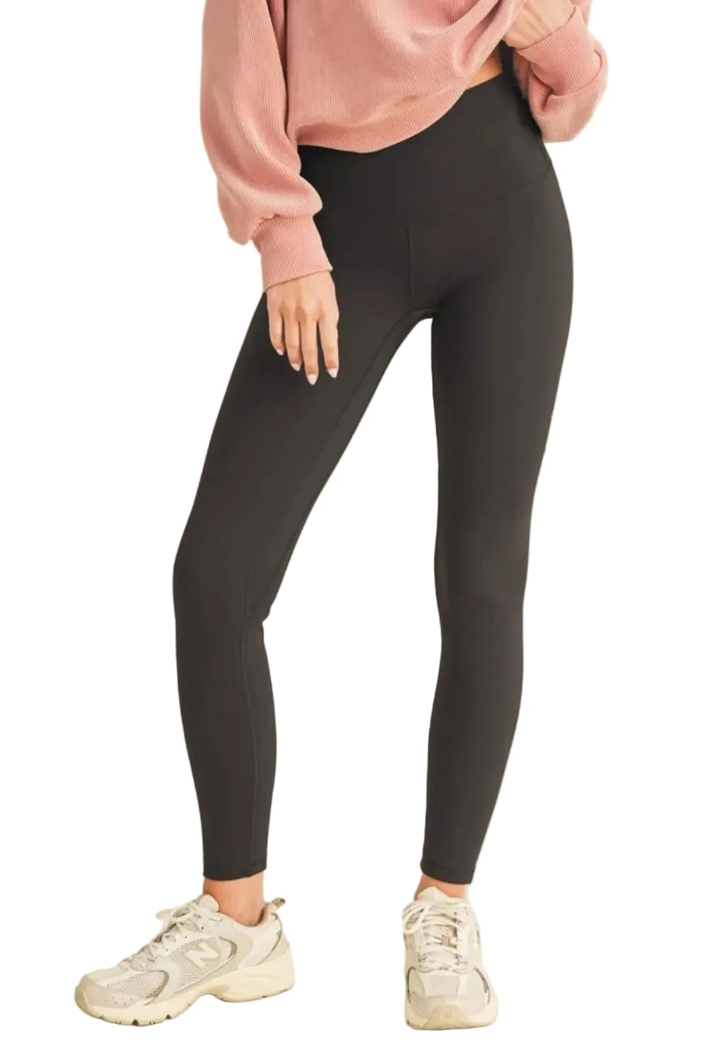 A model wearing high-waisted black leggings, a dusty pink sweatshirt, and white New Balance sneakers, standing against a solid whitebackground.