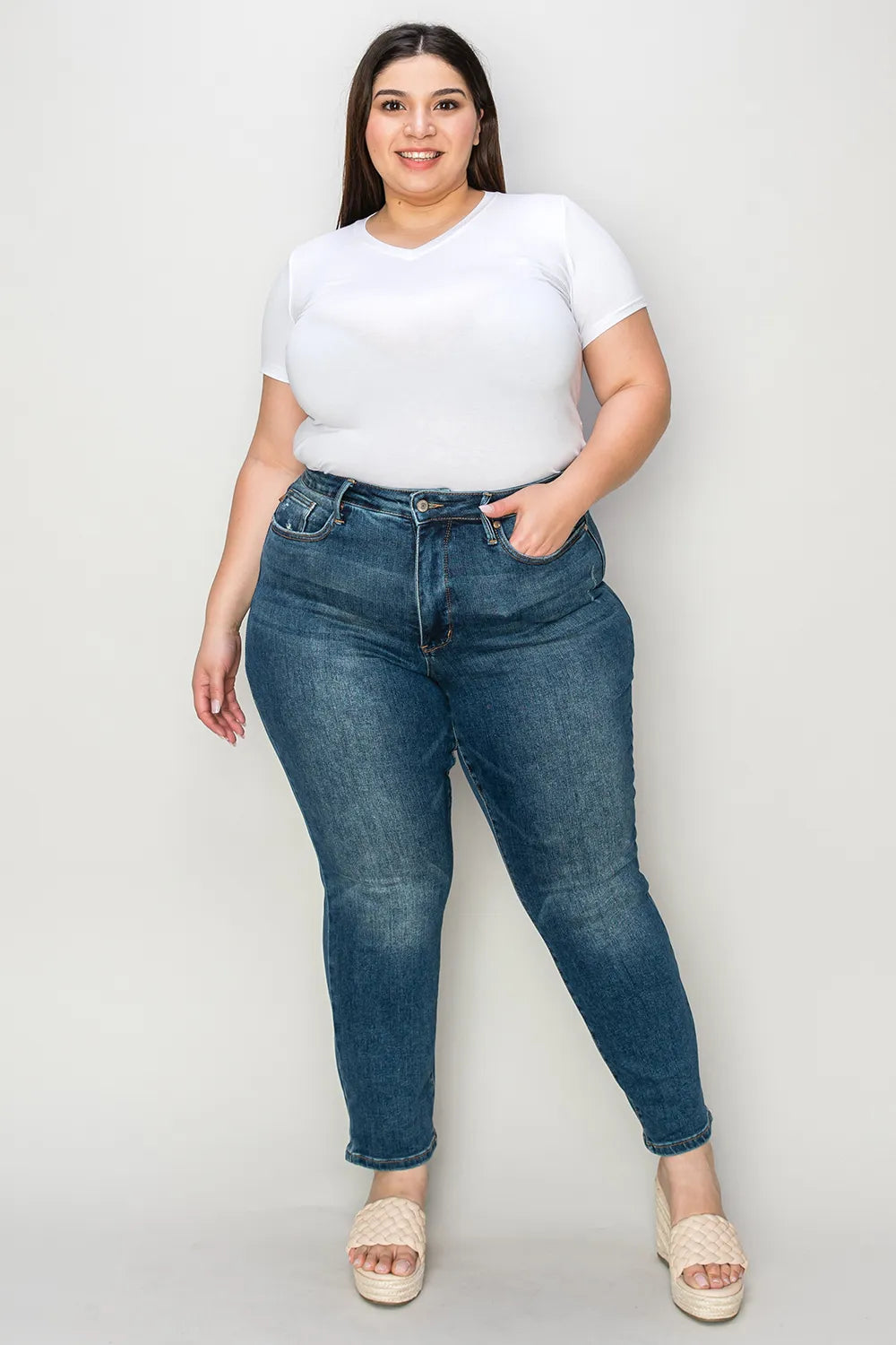 Woman wearing a white t-shirt and blue jeans against a plain background